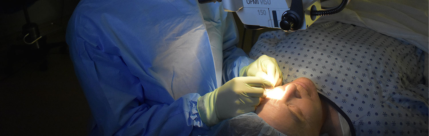A doctor performing cataract surgery on a patient in cap and gown.