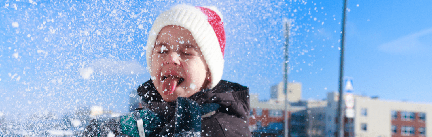 Young child in winter clothes catching snowflakes on their tongue