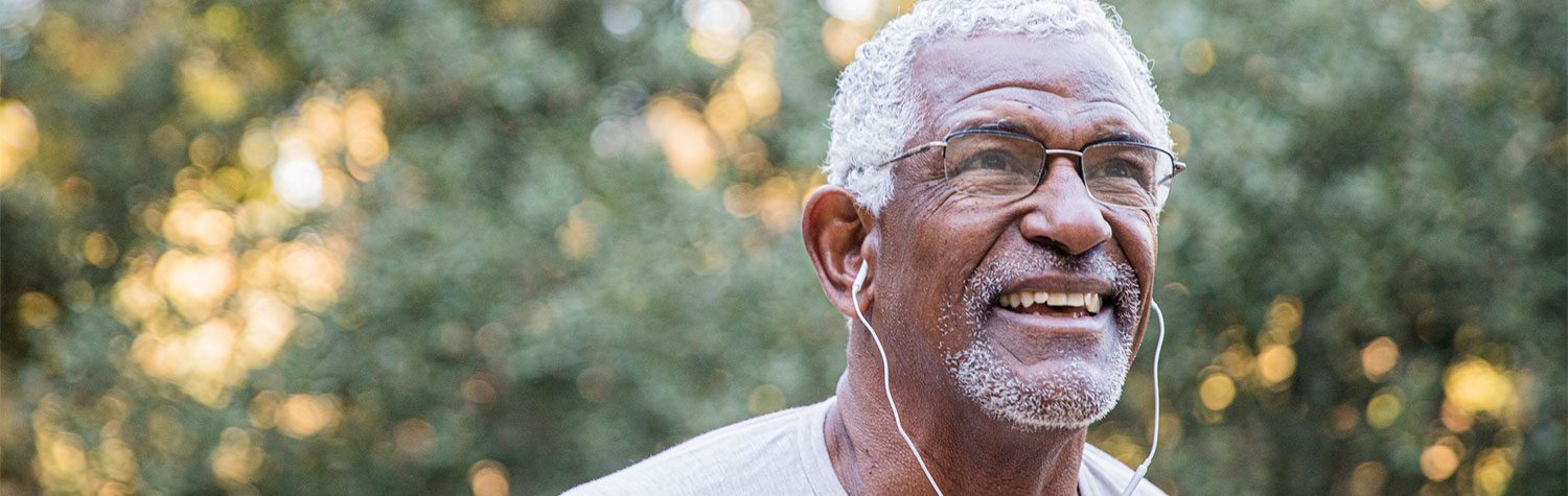 A senior man outdoors with headphones in.