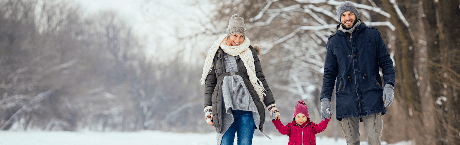 Man, woman, and young child in winter clothes walking together and holding hands in a forested setting