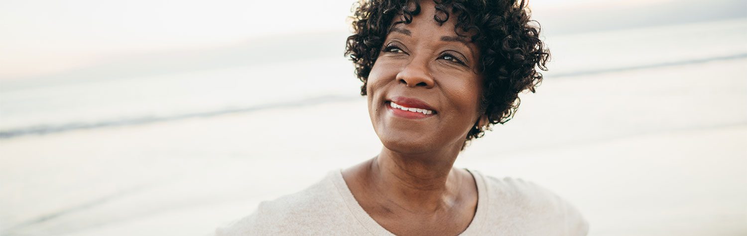 Older woman looking off to her right while smiling and standing on the beach