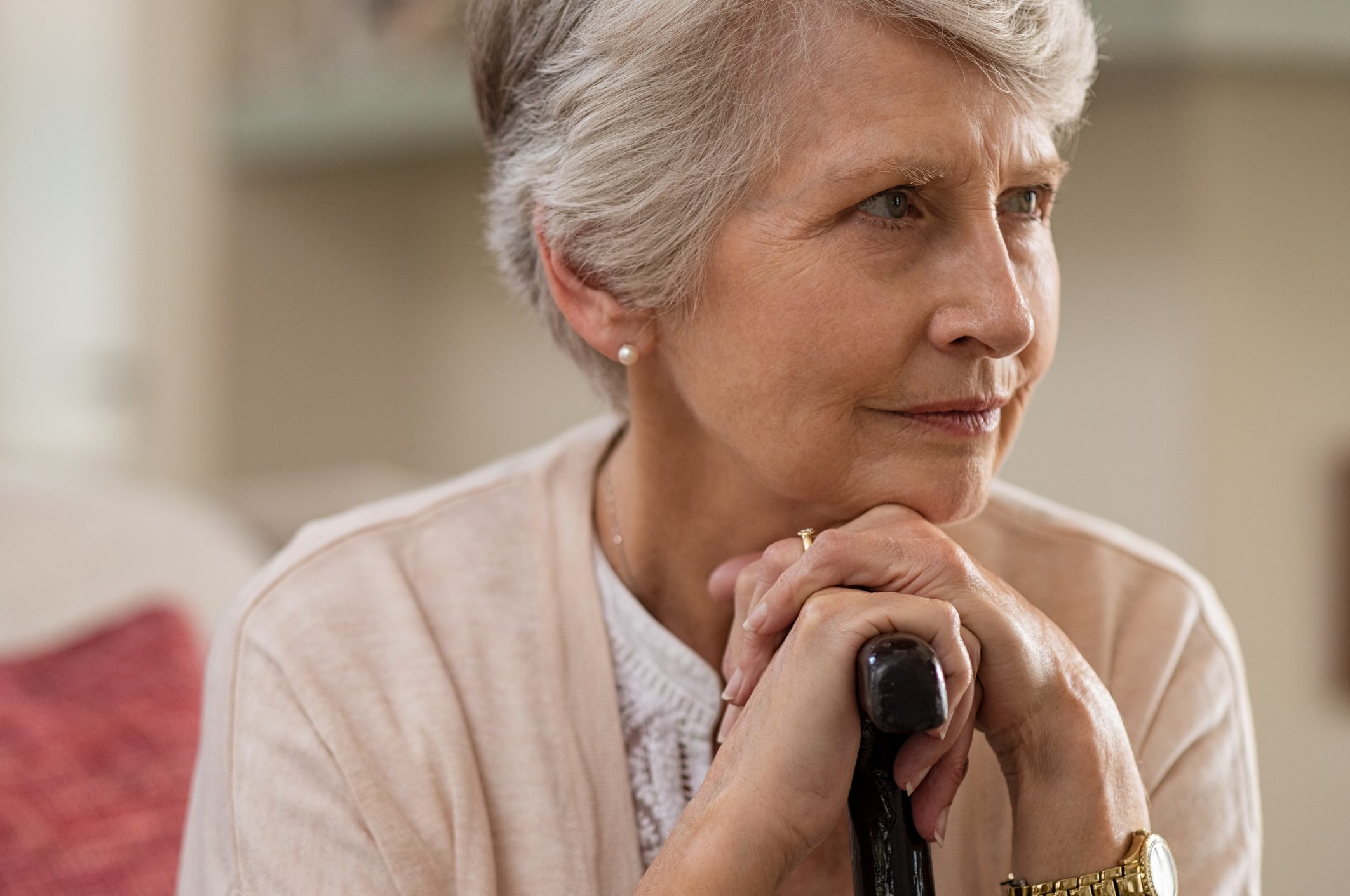 An elderly woman resting her chin on her cane and looking thoughtfully off to the left
