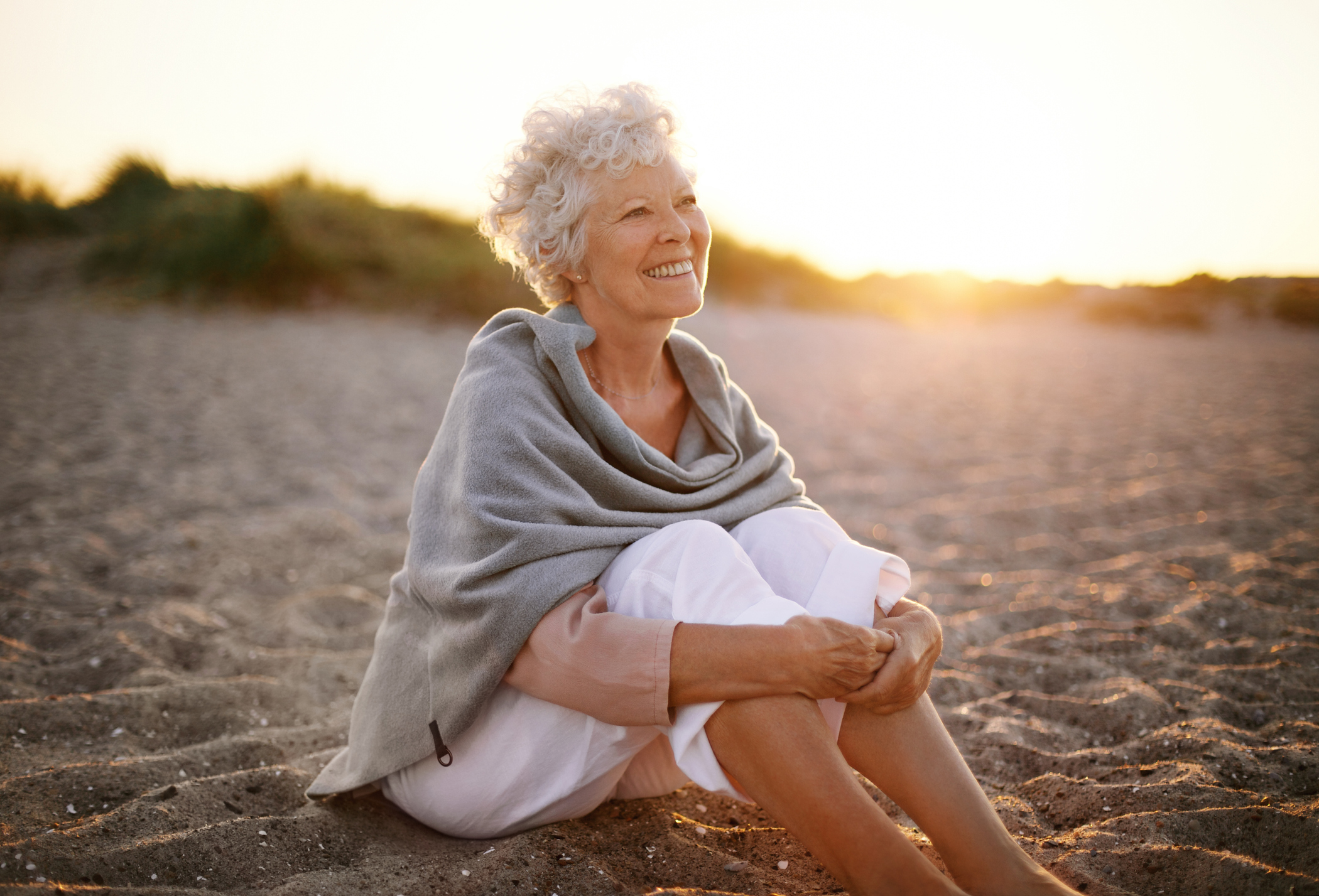 An elderly smiling woman sitting on the beach