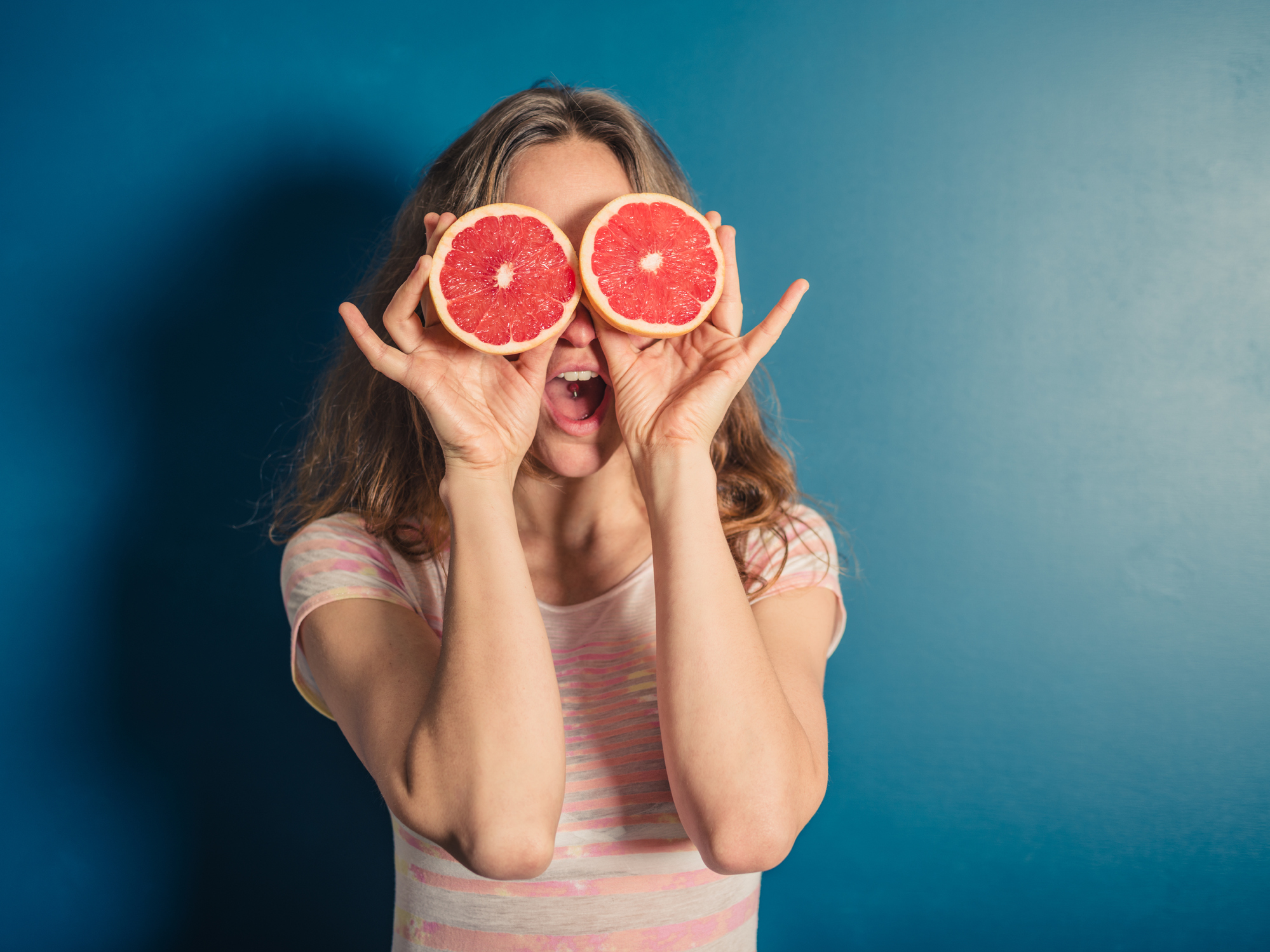 A woman holding sliced grapefruit over her eyes as if they were a pair of glasses.
