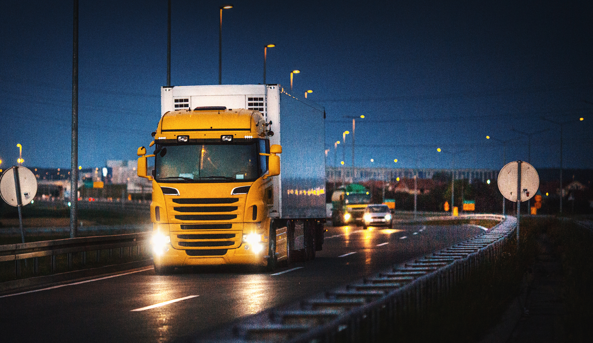 A yellow cargo truck driving on a highway at late sunset