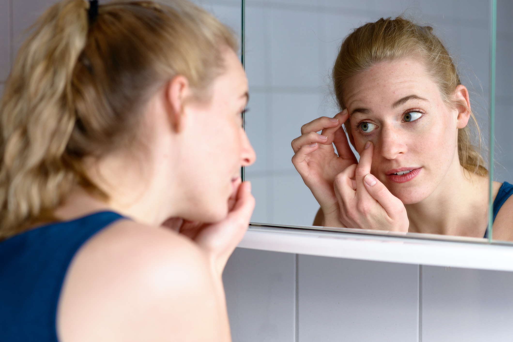 A woman using a mirror to apply a contact lens