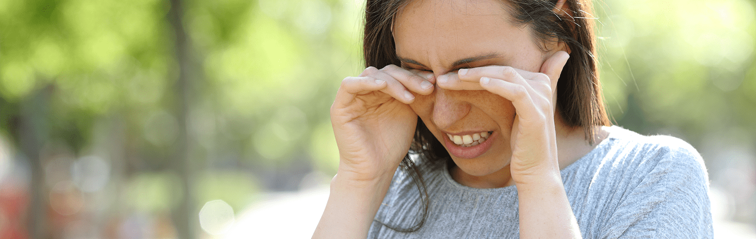 Woman standing outdoors with her hands over her eyes in distress