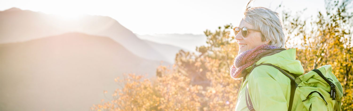 Senior woman hiking in sunglasses with mountains in the background.