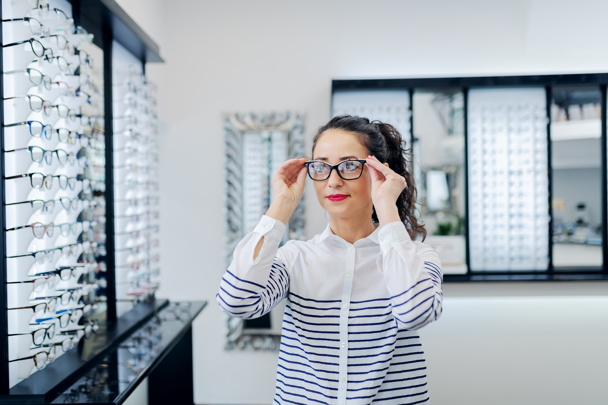 A woman trying on pairs of glasses in a glasses shop.
