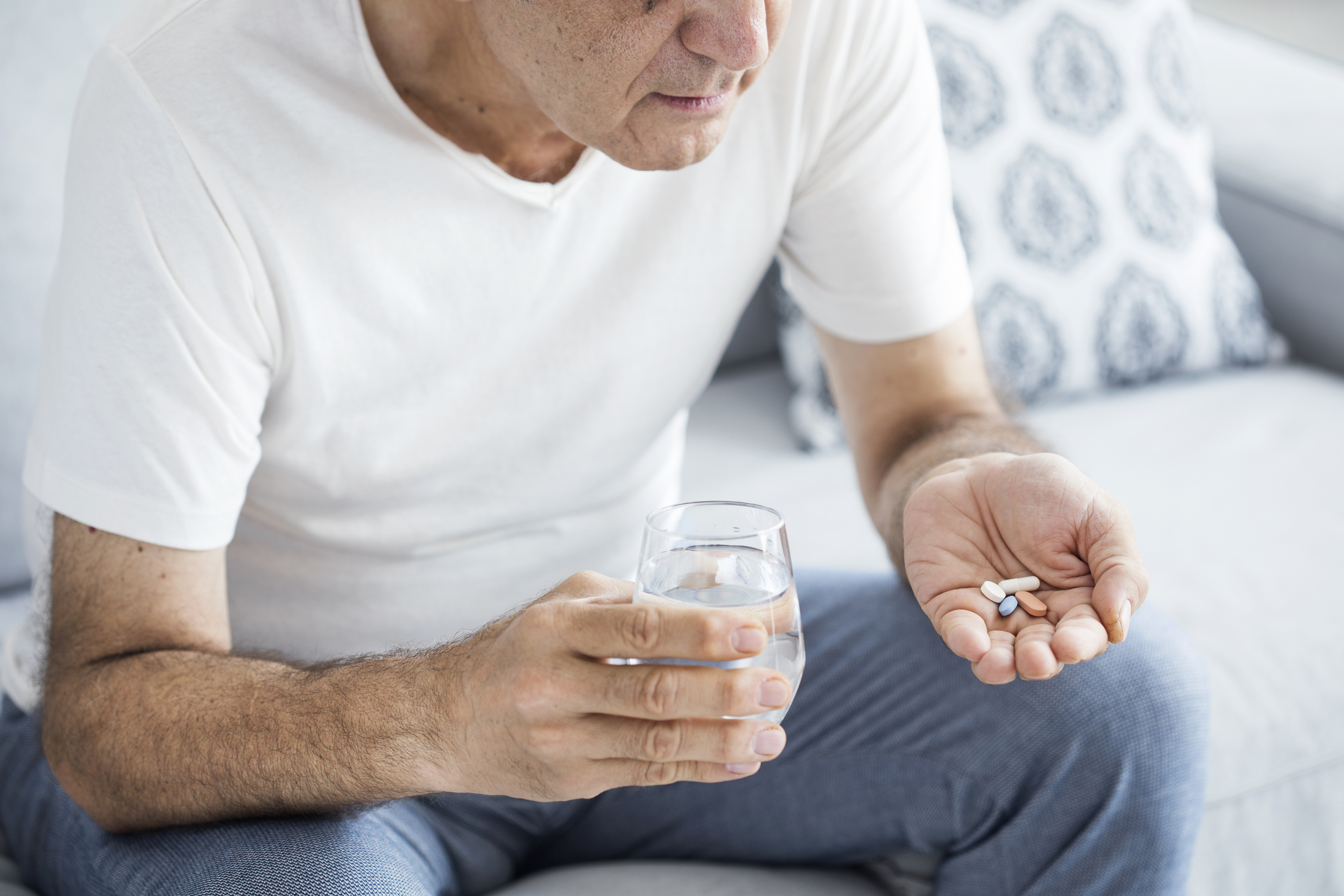 An elderly man holding a glass of water and handful of pills