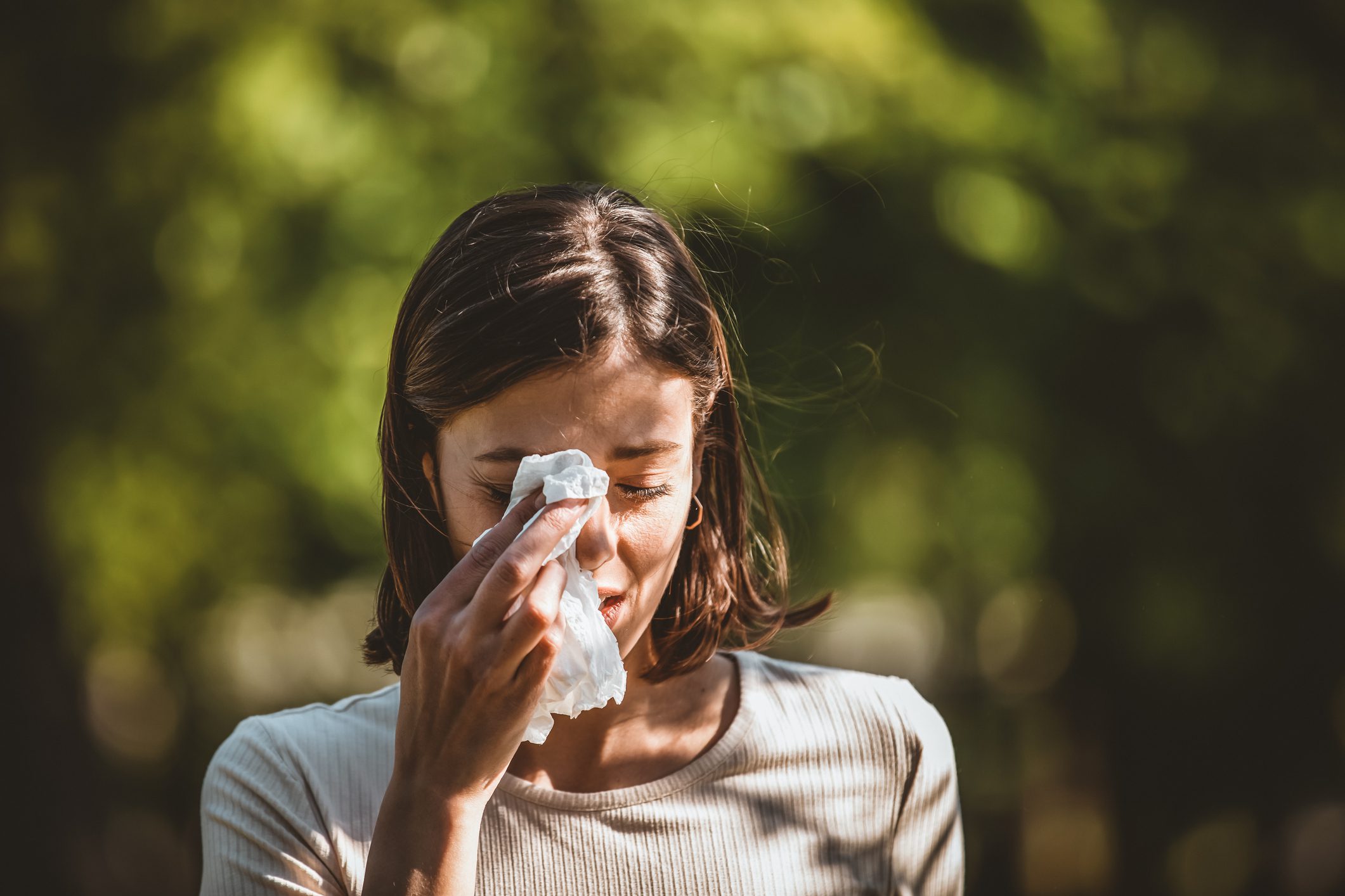 A woman outdoors rubbing her eye with a handkerchief