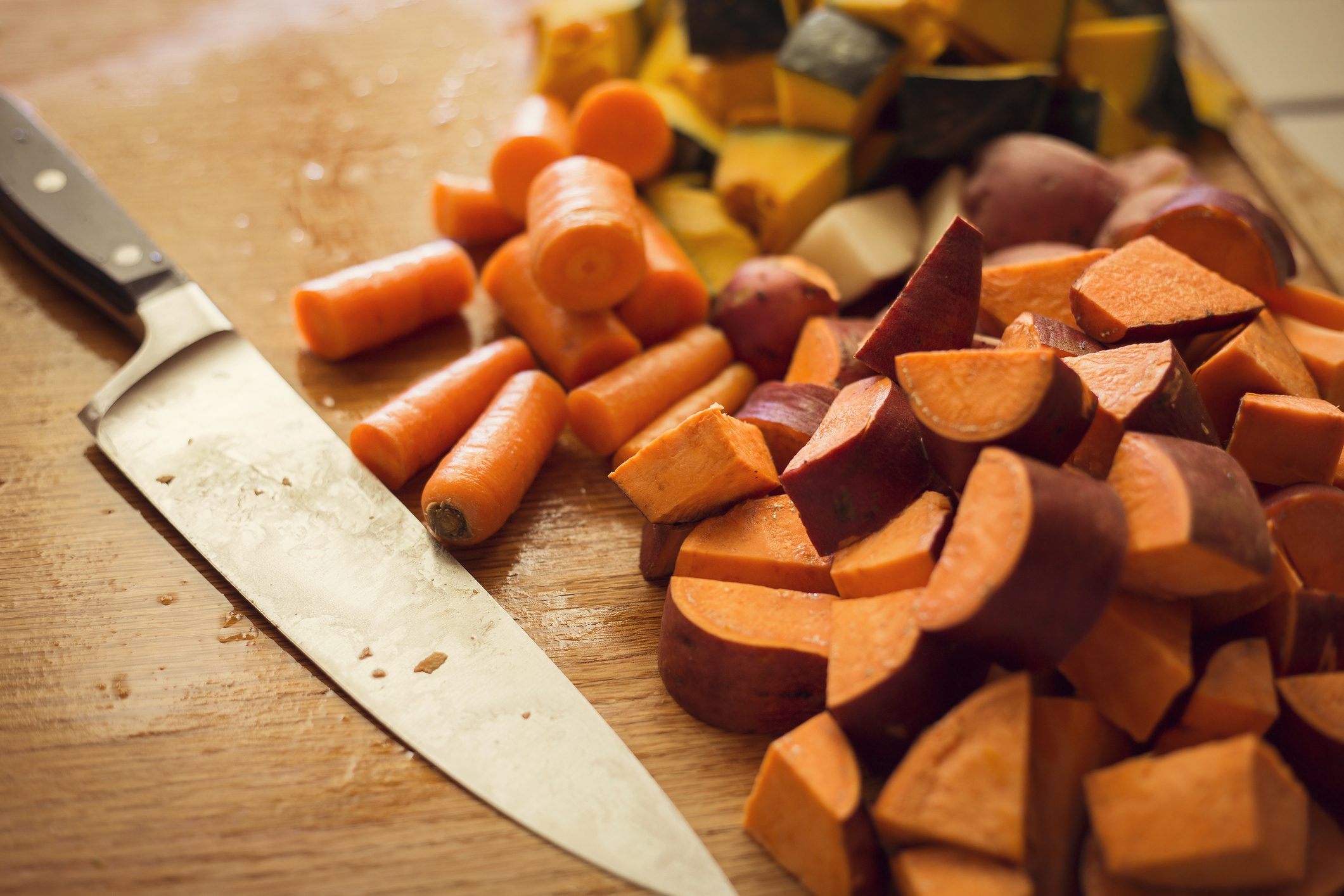 Close up of chopped sweet potatoes and carrots next to a knife on a wooden cutting board