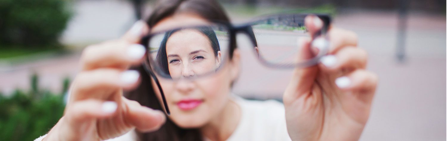 Blurry young woman holds up a pair of eye glasses, through which you can see her face clearly