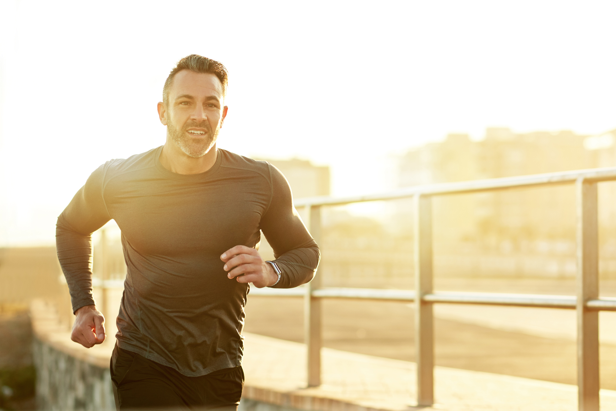 A man running during sunrise outdoors next to an elevated railing.
