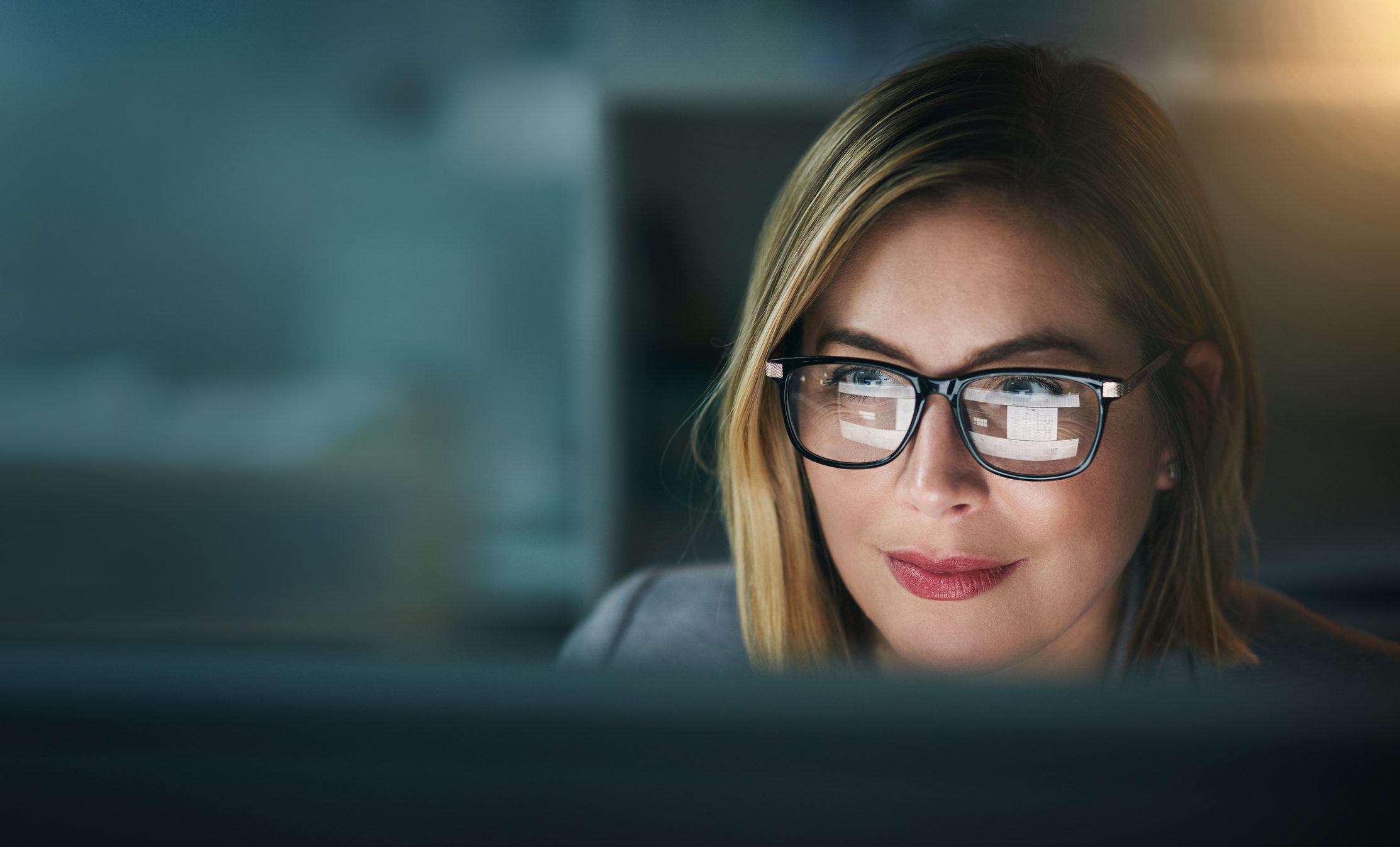 A woman looking at a computer screen, which is reflected in her glasses