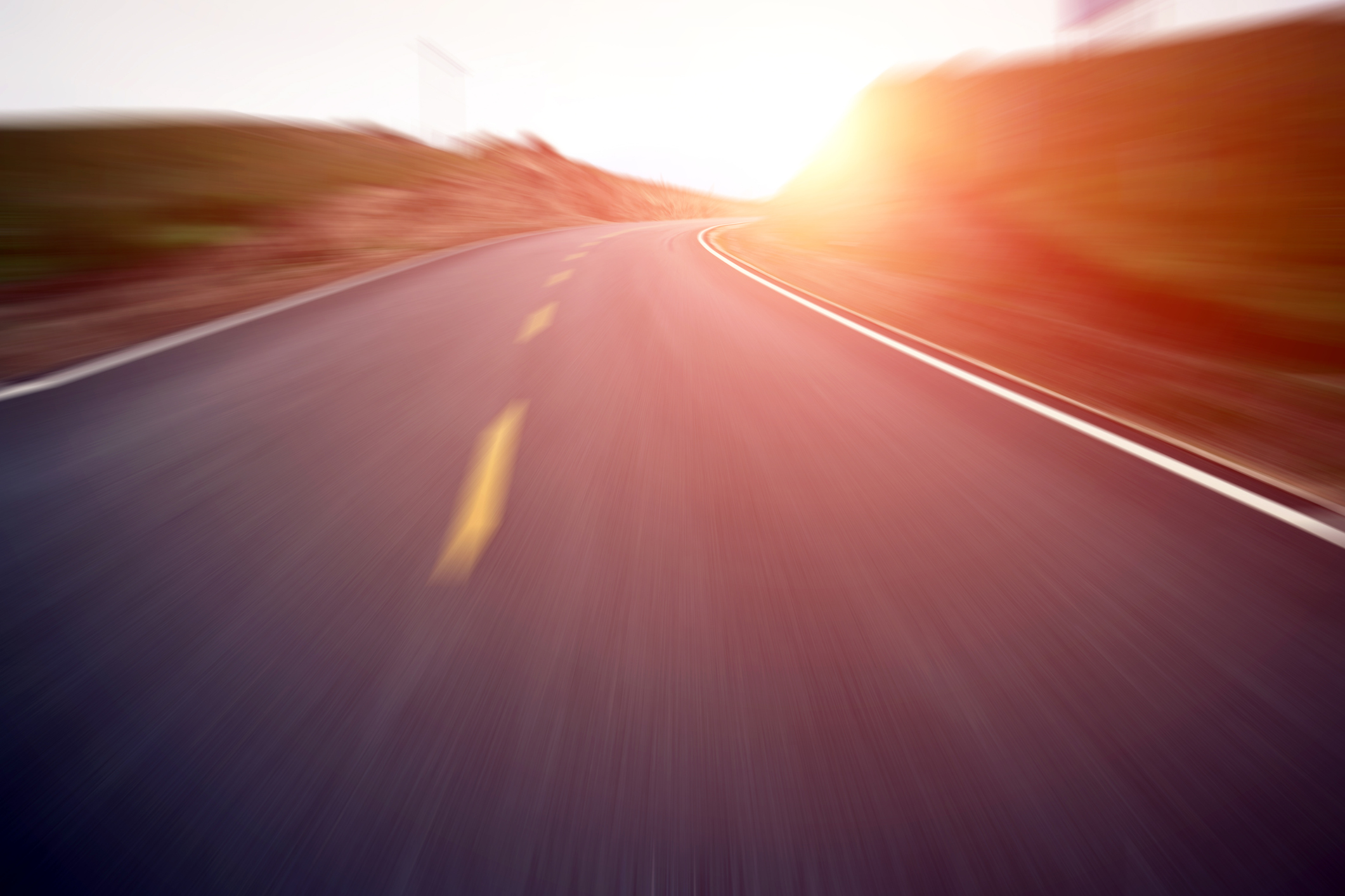 A motion blurred view of a road with the sun low on the horizon