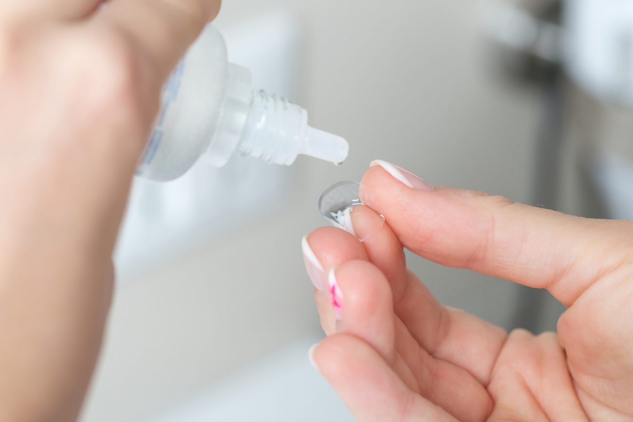 A closeup of hands applying solution to a contact lens