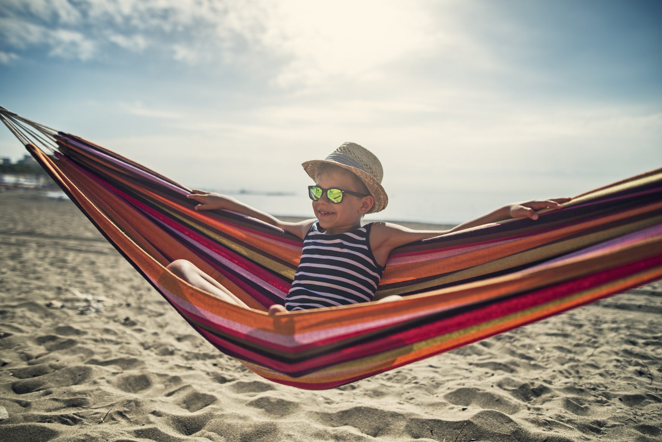 A child in sunglasses sitting in a hammock at the beach