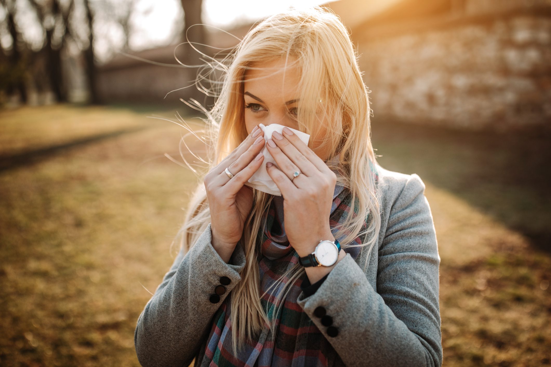 A blonde woman blowing her nose in an outdoor setting