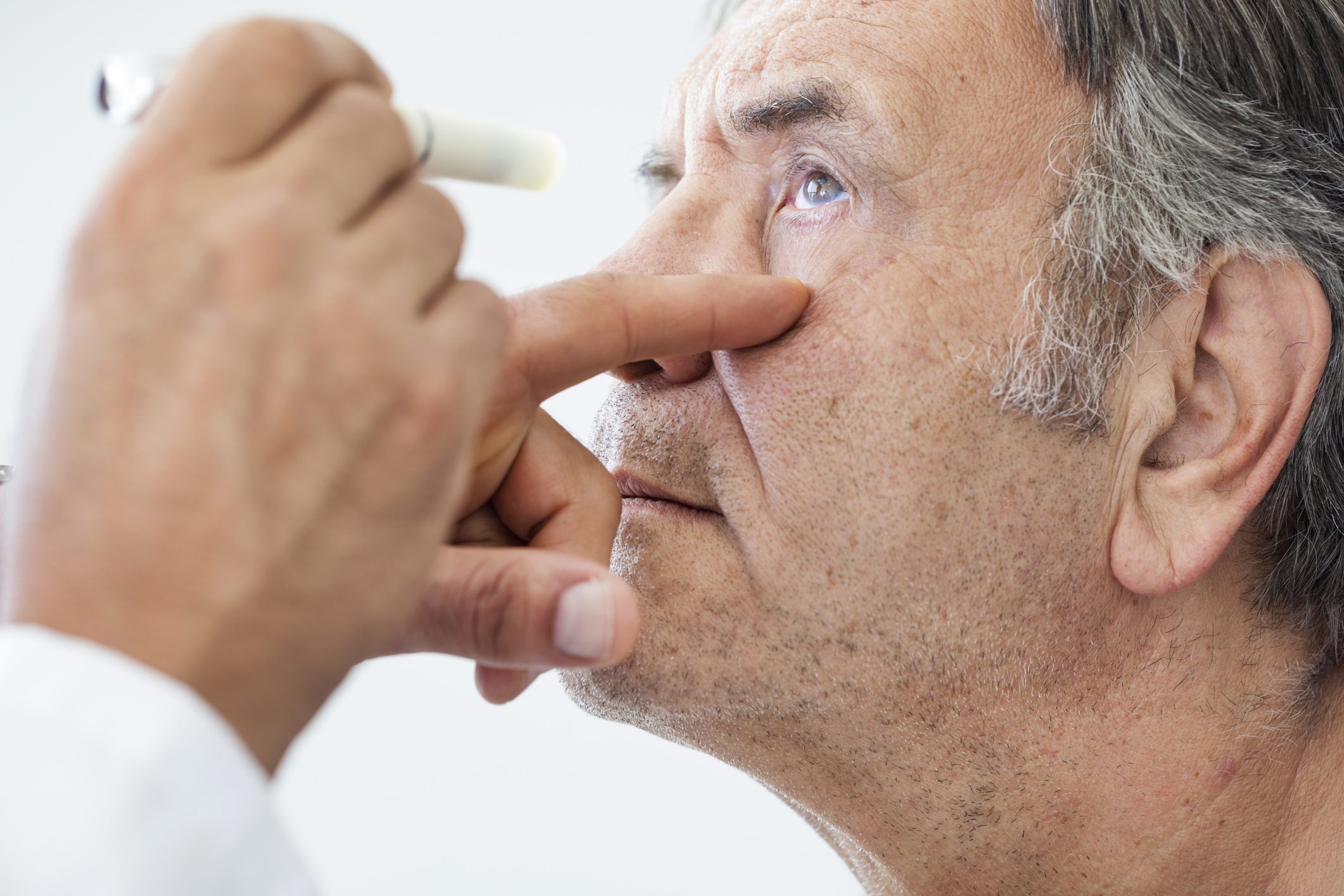 An elderly man being examined by an ophthalmologist who is shining a light in his eye.