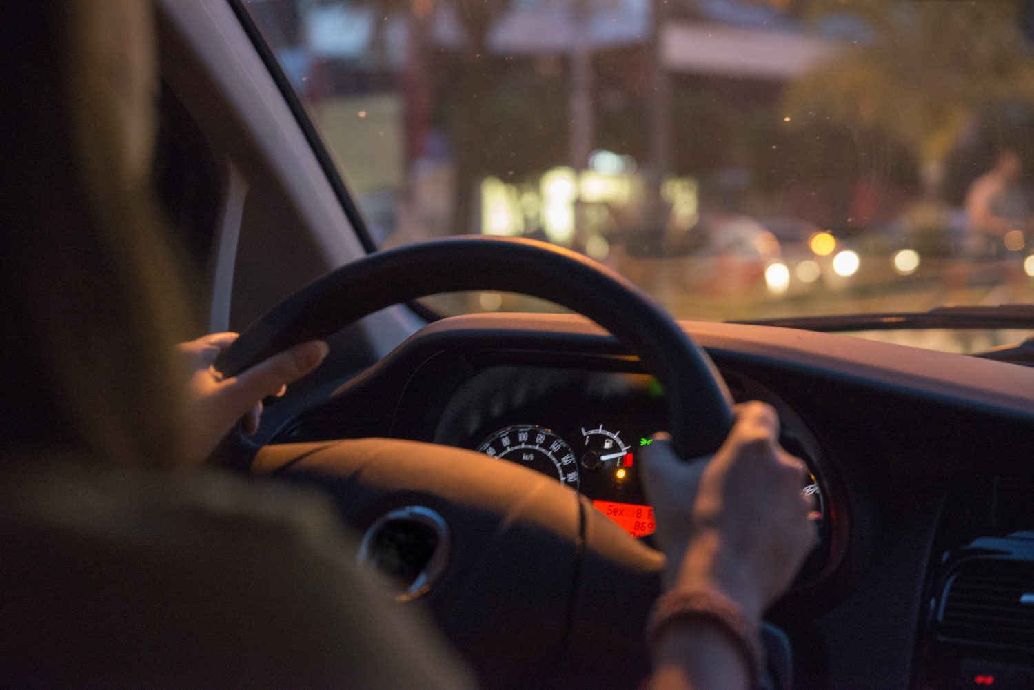 A woman driving at night with her hands on the steering wheel of the car.