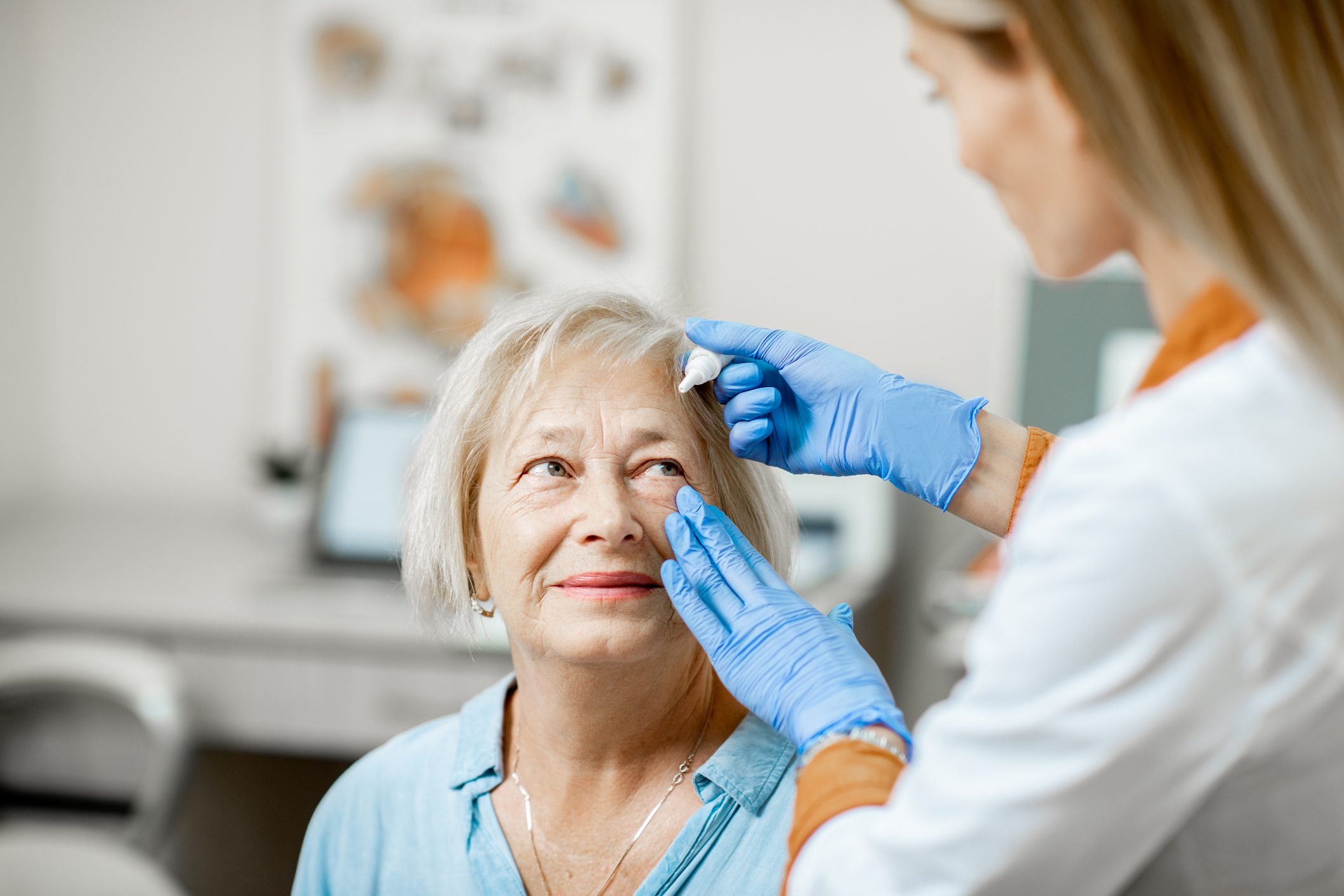 A female doctor applying eyedrops to an older woman's eyes.
