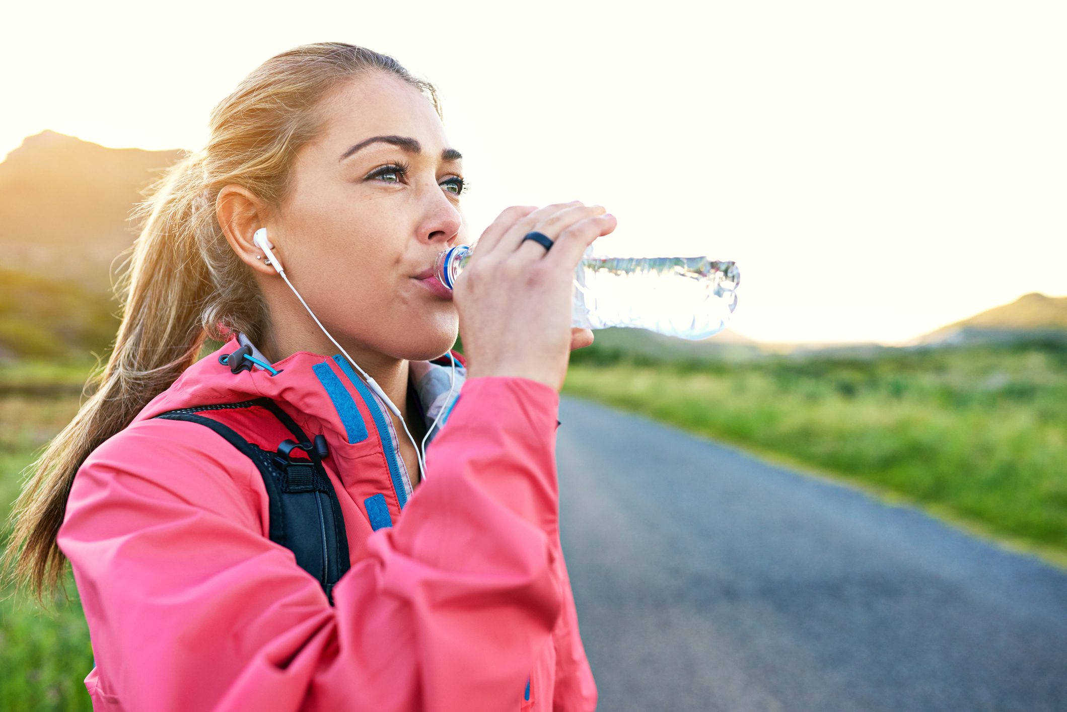 A young woman in a pink jacket taking a sip from her water bottle during her outdoor workout