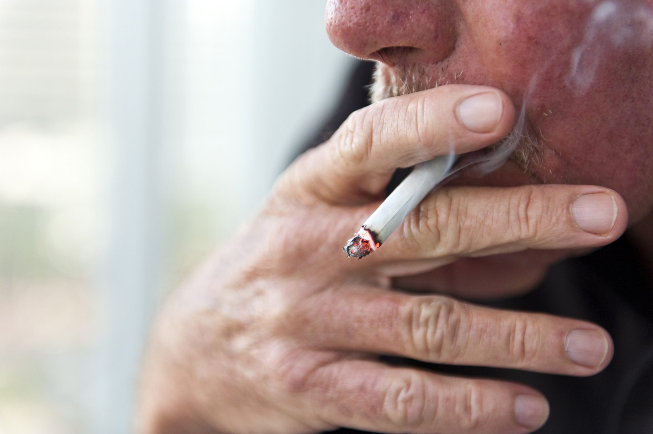 Close up of a mustachioed man smoking a lit cigarette.
