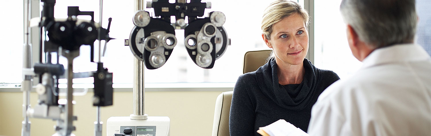 A woman having a conversation with an eye doctor next to eye examination equipment.