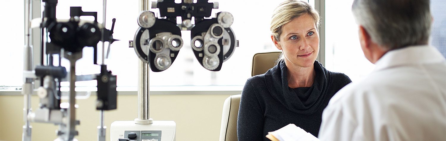 A woman listening to a male doctor in an exam room filled with eye equipment.