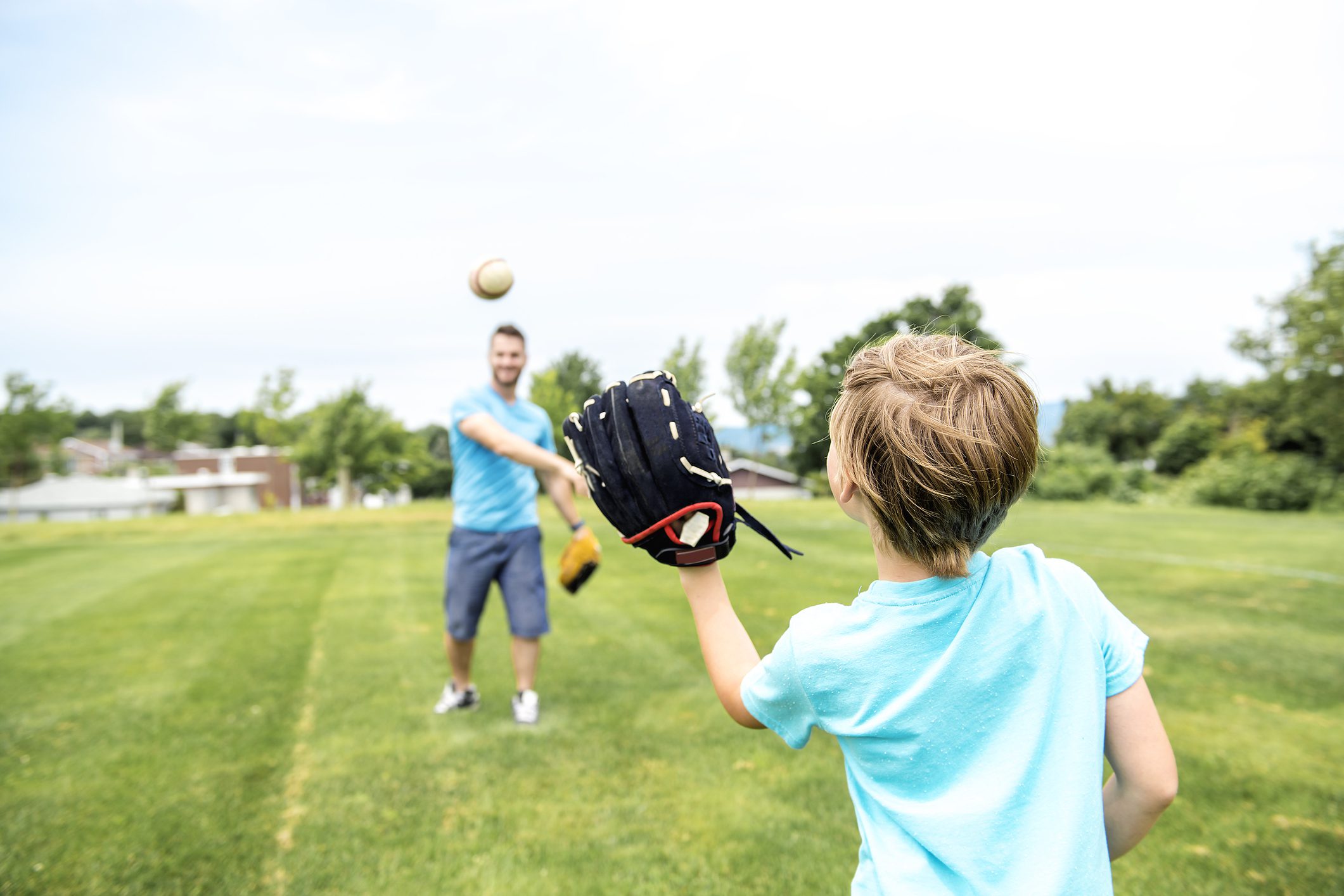 A father throws a ball to his son while playing catch in a grassy field.