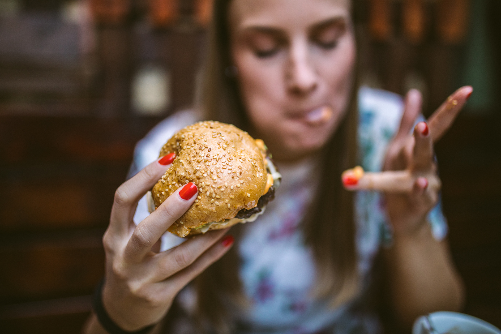 A woman eating a burger and licking cheese off of her finger.