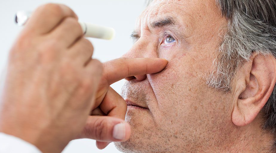 An older man having his eye examined by a doctor holding a light