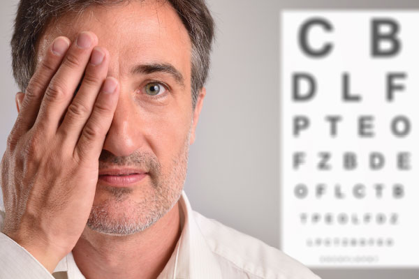 A man standing in front of an eye chart and covering one eye.