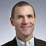 Headshot of a short-haired man in a suit smiling in front of a white background