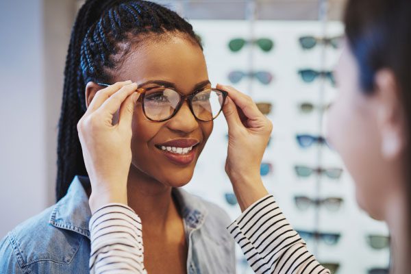 A salesperson placing glasses on a woman's face.