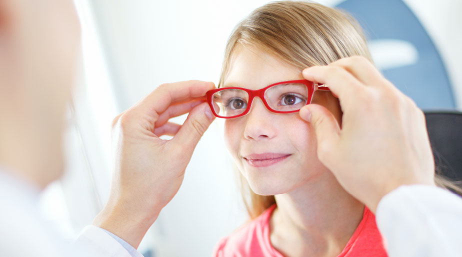 A doctor placing red eyeglasses on a child