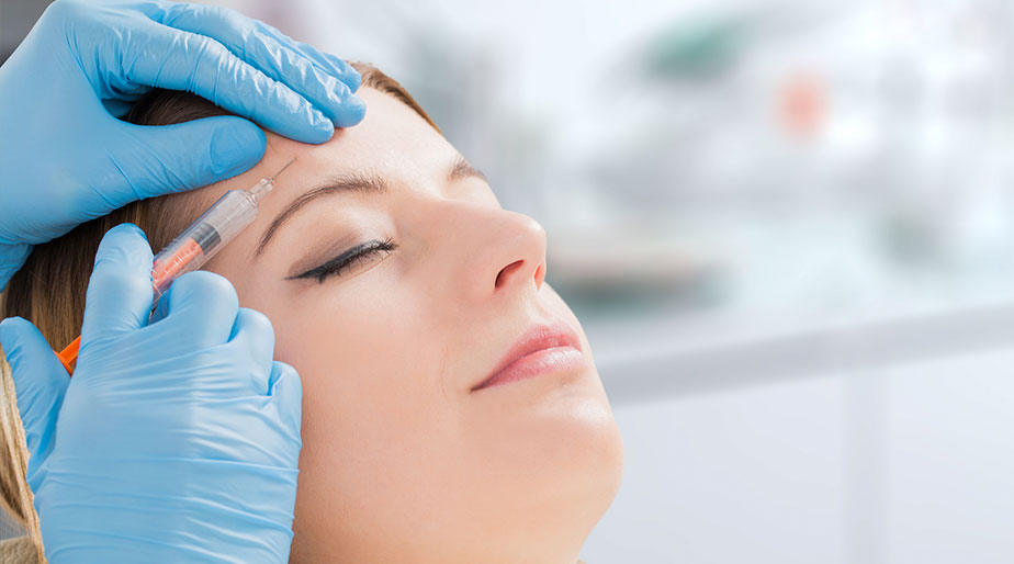 A doctor performing a facial filler procedure on a woman's forehead