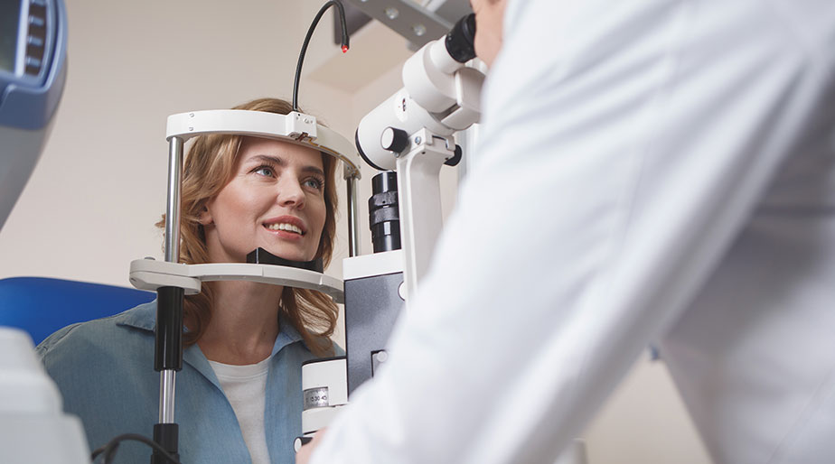 A woman having her eye's examined by a doctor standing behind a microscope.
