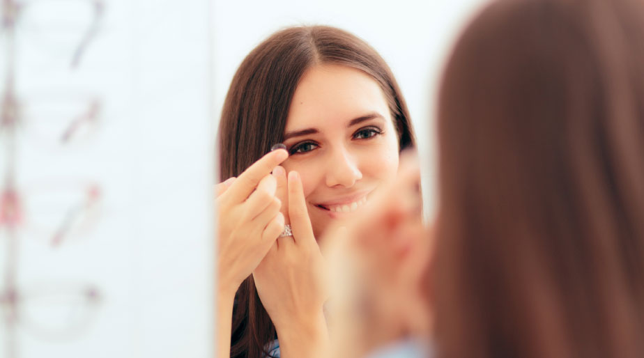 A woman using a mirror to apply a contact lens.