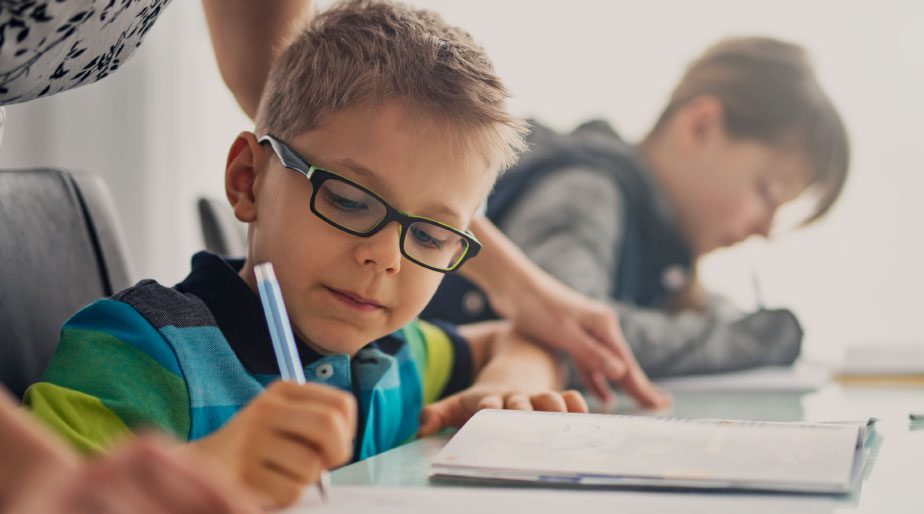 A woman helping a child wearing glasses with their schoolwork.