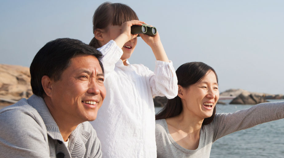 A child with her family standing on a beach and looking through binoculars.