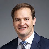 Headshot of a man in a suit smiling in front of a gray background