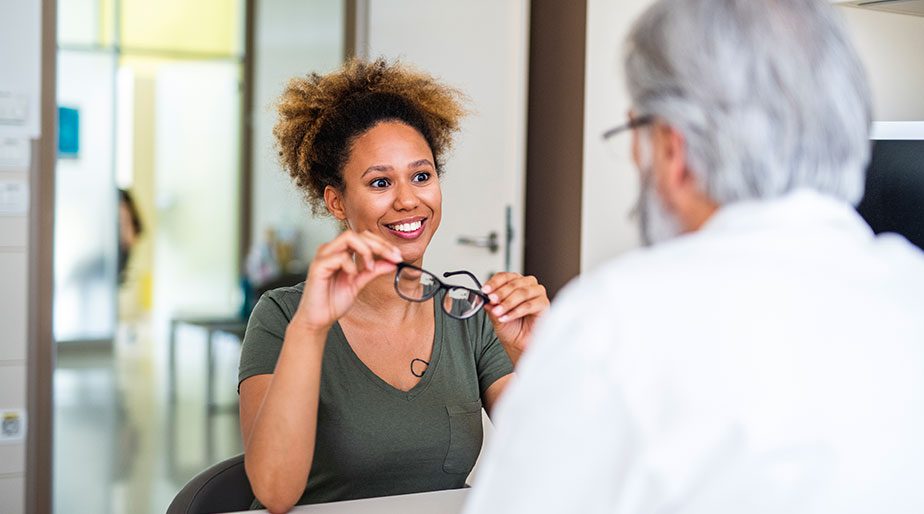 A woman holding glasses and speaking with a doctor