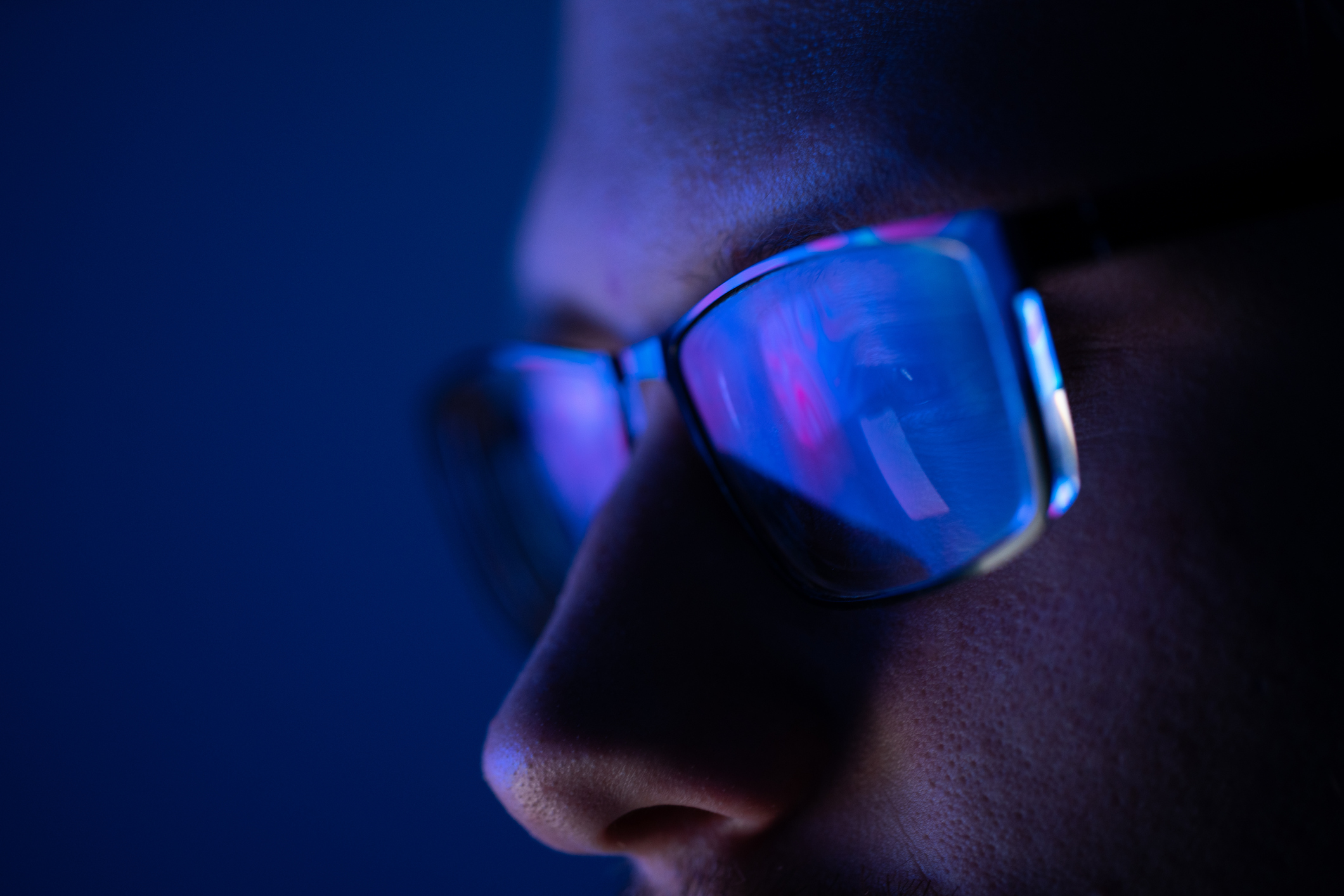 A closeup of a man wearing glasses reflecting the light of a screen.