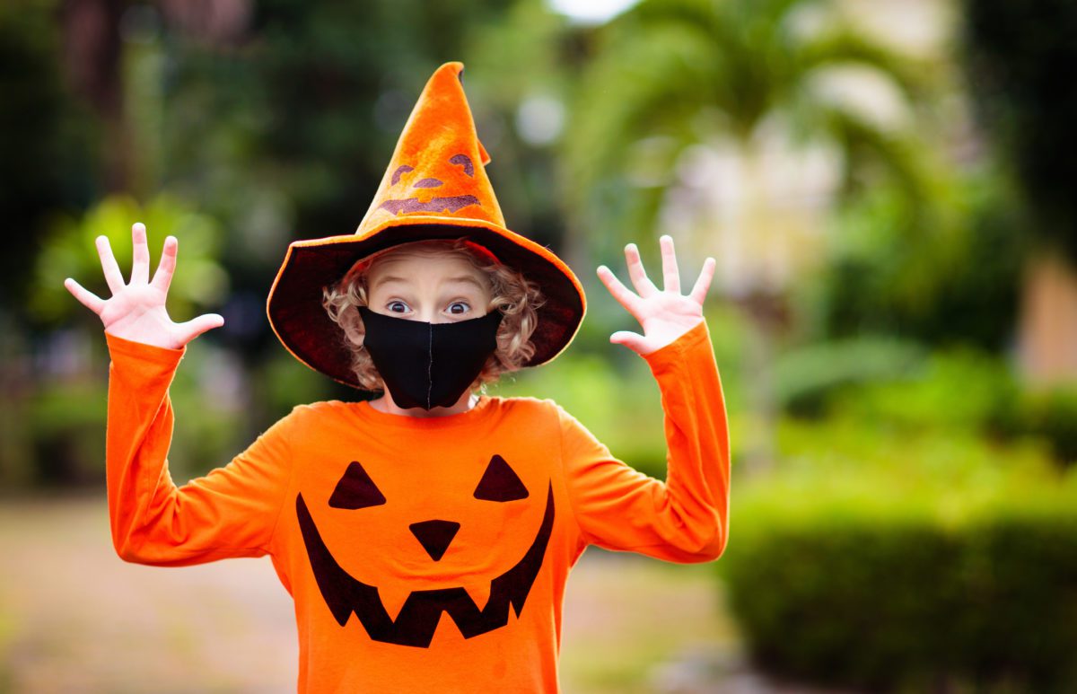 A child wearing an orange jack-o-lantern shirt, a pointe orange jack-o-lantern hat, and a black mask