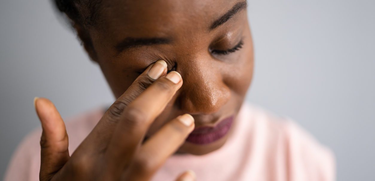 Close up of woman in a pink shirt tiredly rubbing her eye with her hand