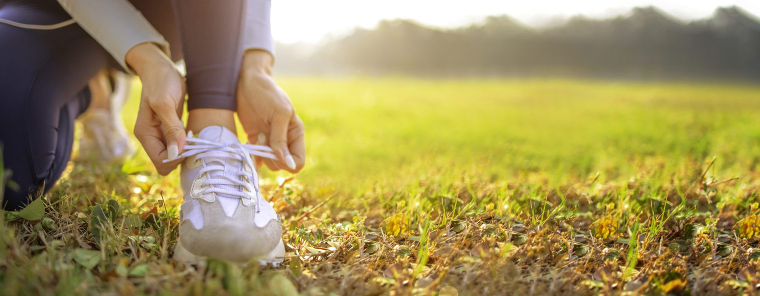 Close up stock image of a woman kneeling in a field and tying her brown and white sneaker