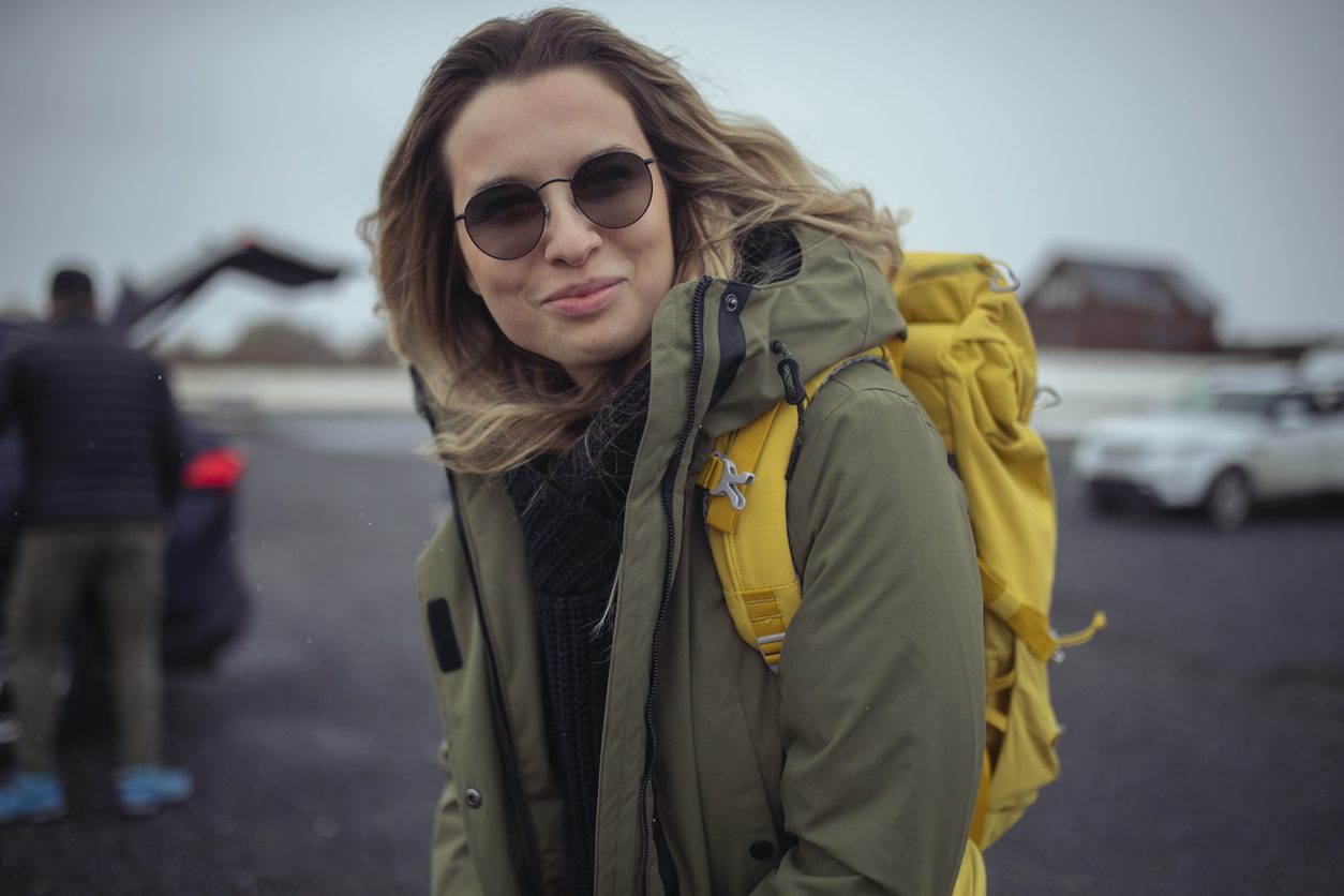 woman in jacket wears sunglasses and a backpack